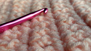 Close-up of a delicate dusty rose crochet scrunchie resting on soft cream fabric.