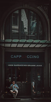 Man enjoying coffee outdoors in casual yet refined attire.