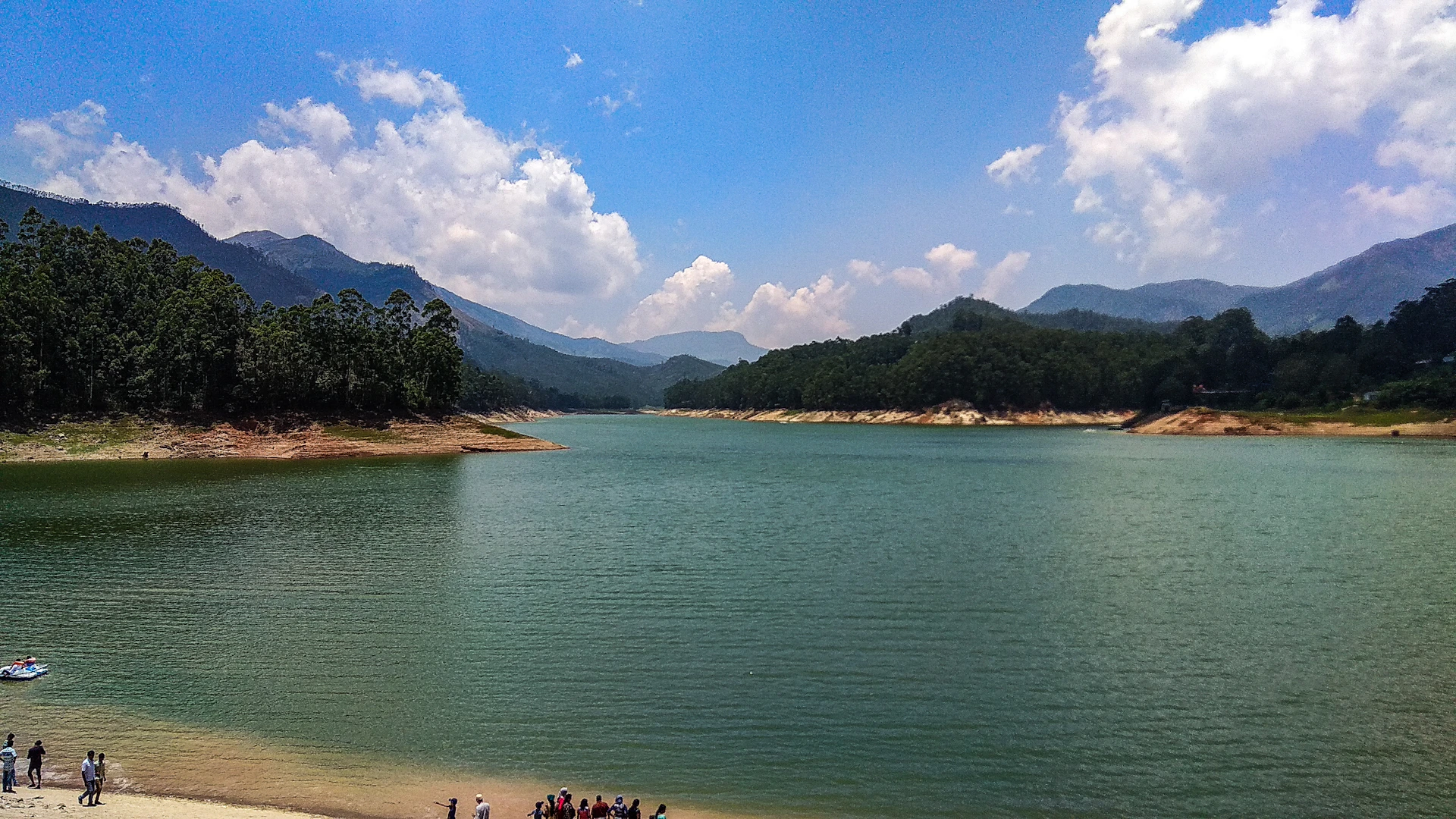 people swimming on sea near mountain under blue sky during daytime