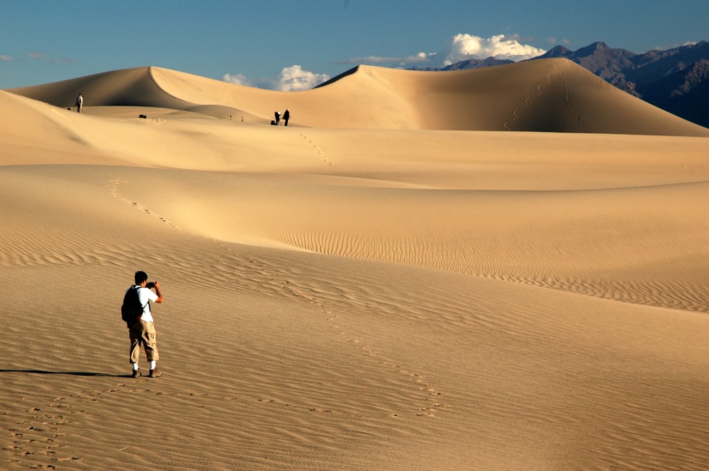 man in white shirt walking on desert during daytime