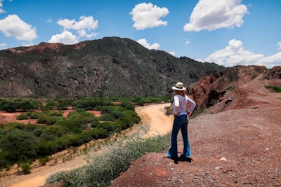 woman in white shirt and blue denim jeans standing on brown dirt road during daytime