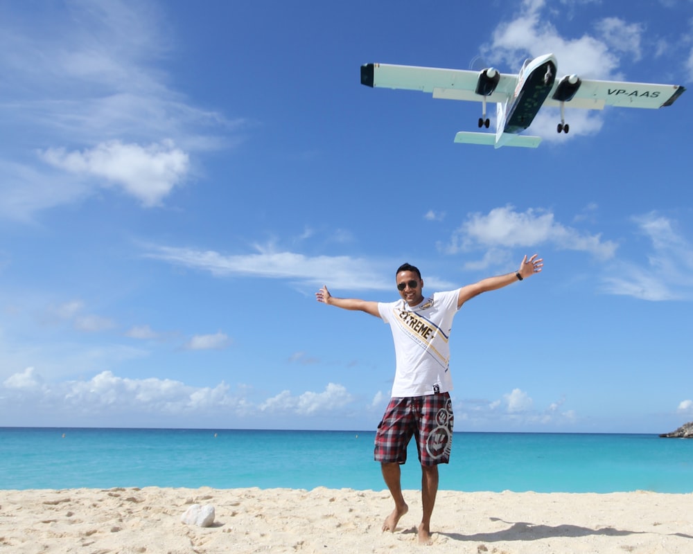 a man standing on a beach with a plane flying overhead