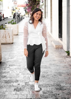 A stylish woman wearing a trendy top and denim, walking down a boutique street.