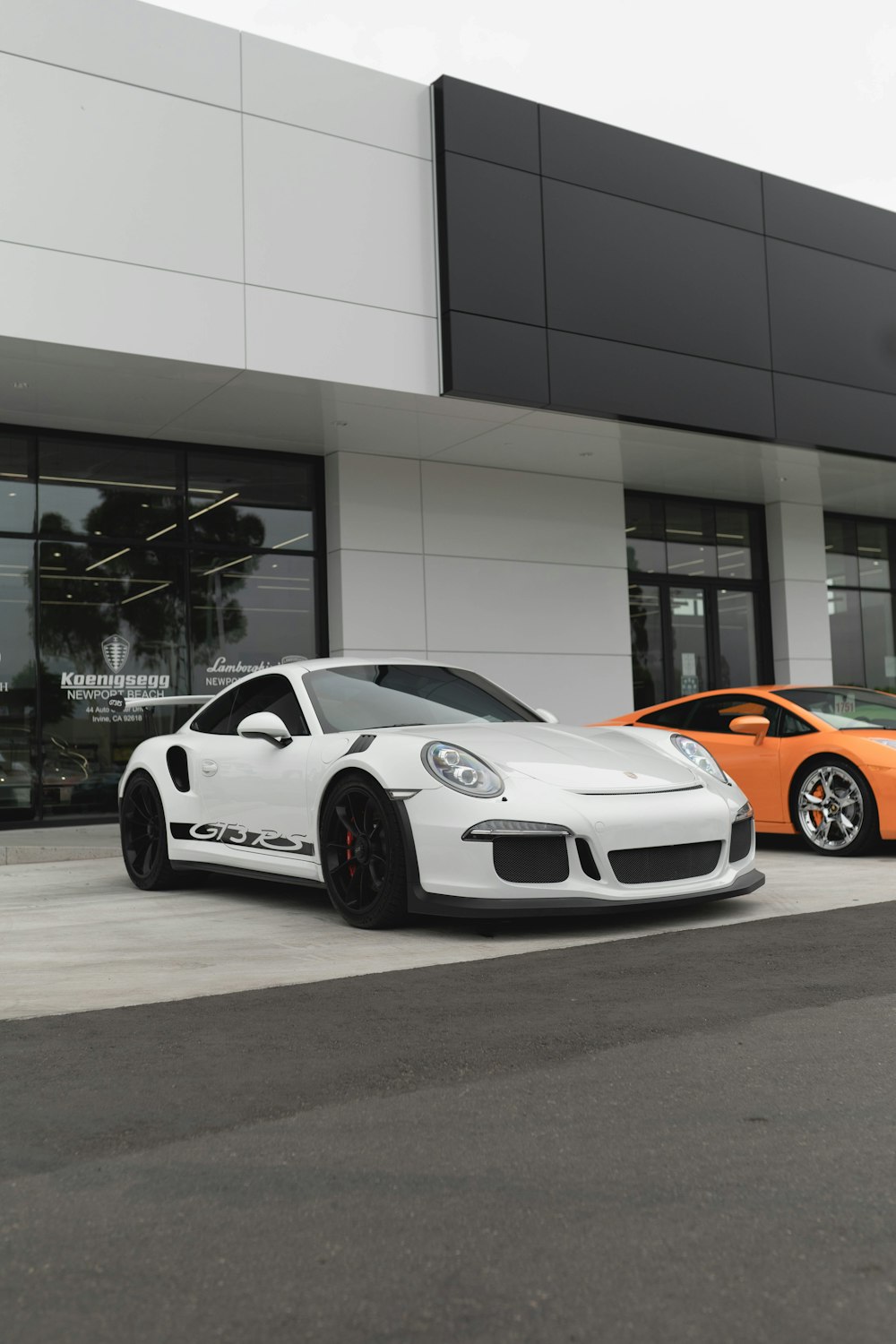 Porsche 911 blanco y naranja aparcado frente a un edificio blanco