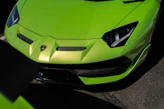 A vibrant green sports car is prominently displayed, showcasing its sleek design and aerodynamic features. The car's sharp, angular headlights and distinctive front grille contribute to an aggressive and modern appearance. The glossy surface reflects light, enhancing its vibrant color.