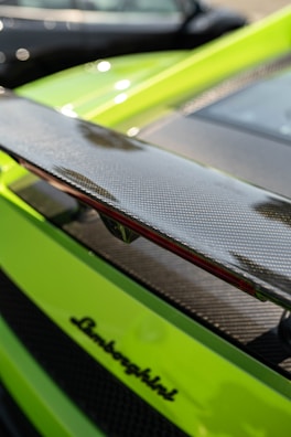 A close-up of a bright green sports car showing its sleek carbon fiber rear spoiler and the black Lamborghini logo.