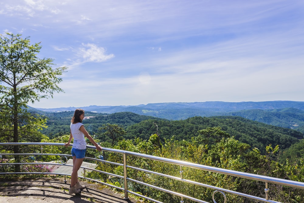 woman in blue tank top and blue denim shorts standing on brown wooden bridge during daytime