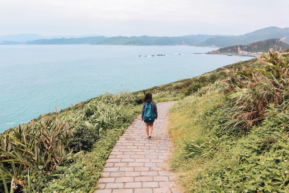 woman in blue shirt walking on pathway near body of water during daytime