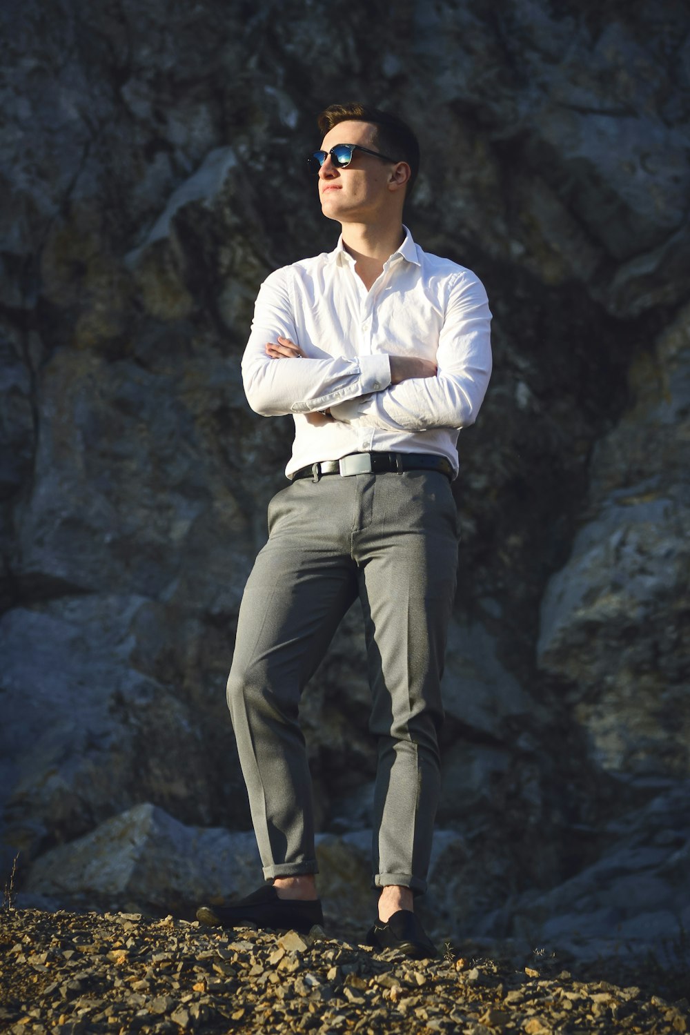 man in white dress shirt and gray pants standing on gray rock