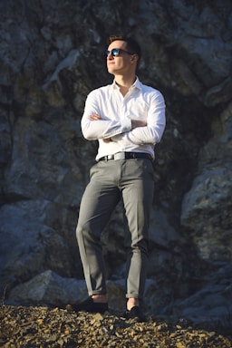 photography poses for men,how to photograph standing man looking far away.; man in white dress shirt and gray pants standing on gray rock