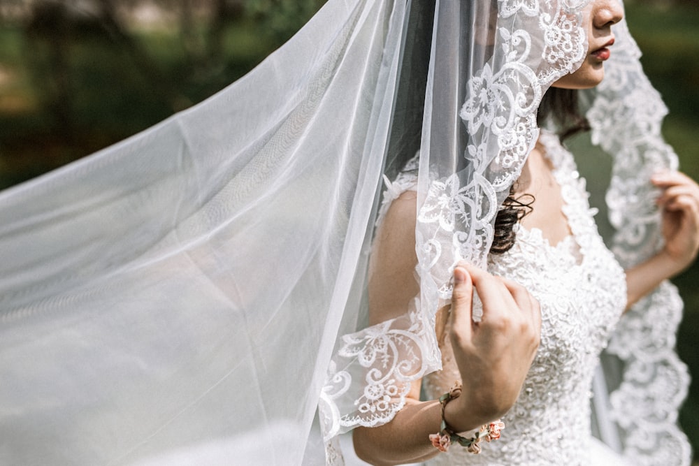 mulher no vestido de noiva branco que segura o véu branco