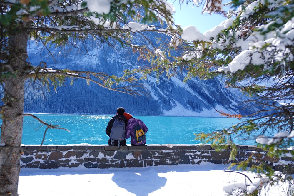 man and woman sitting on brown wooden bench near body of water during daytime