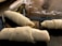 Three uncooked pastry rolls are placed on a dark surface, likely a countertop. There is some flour sprinkled on the surface around the pastries. A pastry cutter or knife is partially visible in the background.