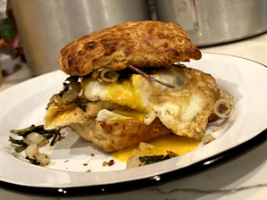 Close-up of a steaming breakfast sandwich with eggs, cheese, and bacon on a toasted bun.