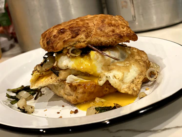 Close-up of a steaming breakfast sandwich with eggs, cheese, and bacon on a toasted bun.