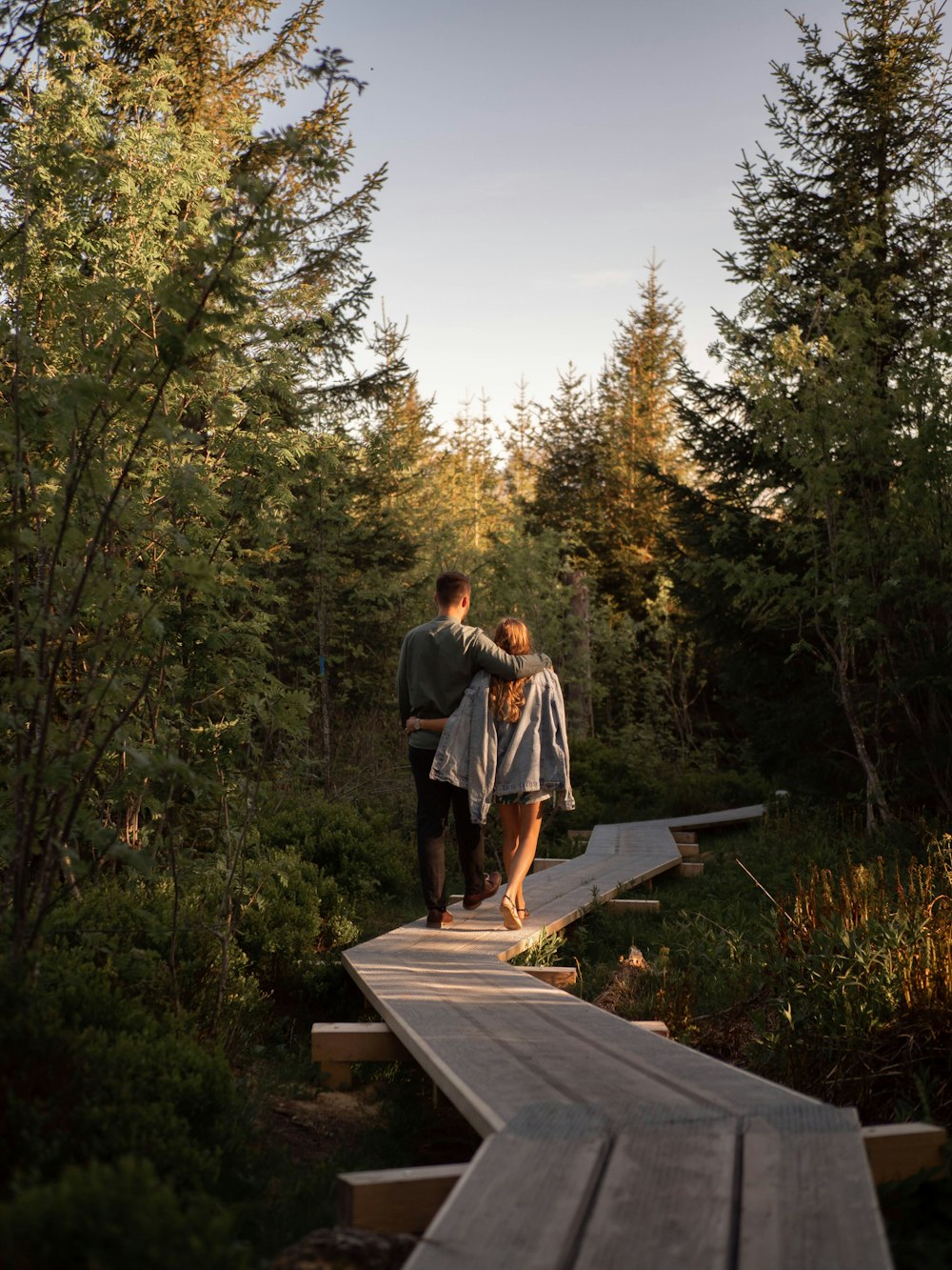 man and woman walking on wooden bridge surrounded by trees during daytime