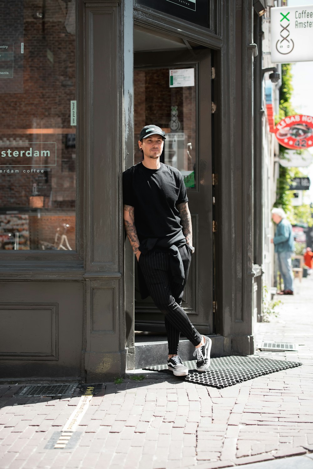 man in black long sleeve shirt and black pants standing beside store during daytime