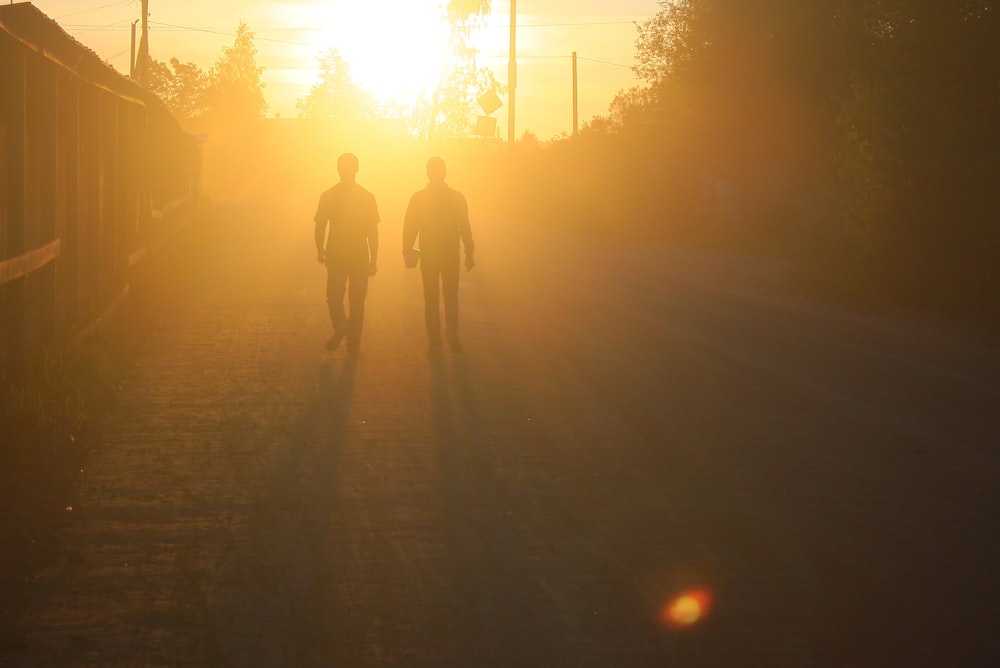 silhouette of 2 person walking on road during sunset