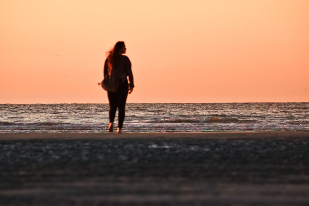 woman in black dress walking on beach during sunset