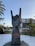 A large stone sculpture of a hand making the 'rock on' gesture is prominently displayed. It is located outdoors with palm trees and a hotel building in the background. The base of the sculpture features a logo and text indicating 'Hard Rock Hotel Tenerife.'