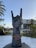 A large stone sculpture of a hand making the 'rock on' gesture is prominently displayed. It is located outdoors with palm trees and a hotel building in the background. The base of the sculpture features a logo and text indicating 'Hard Rock Hotel Tenerife.'