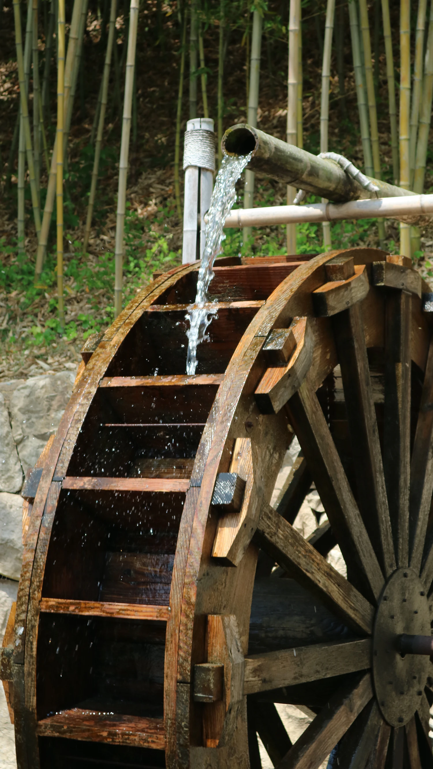 A wooden water wheel with water pouring over its paddles into a timber trough