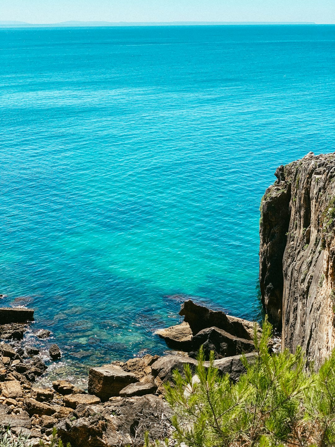 blue sea beside gray rocky mountain during daytime