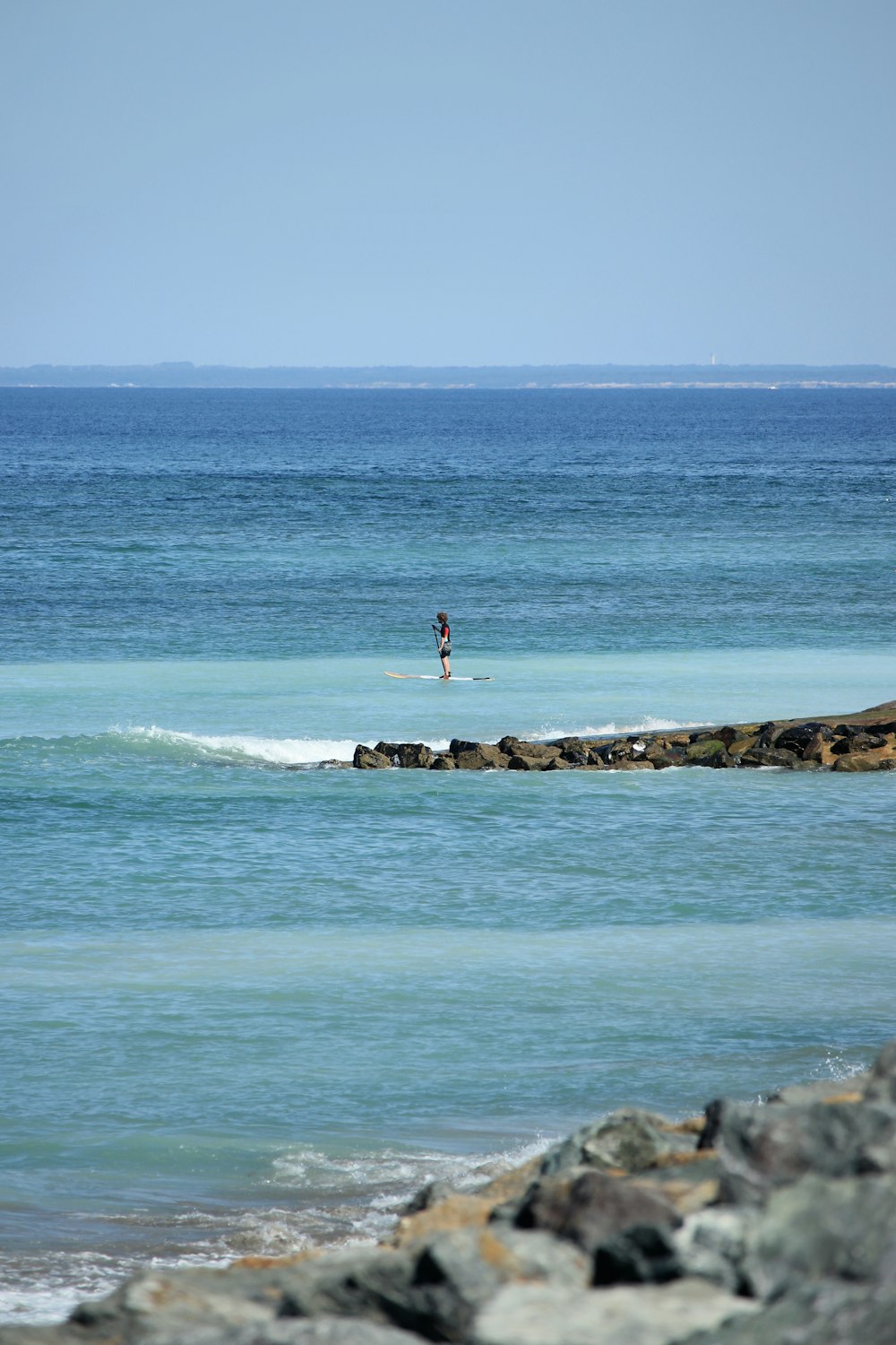 person in red shirt and black shorts standing on rock formation in front of ocean water