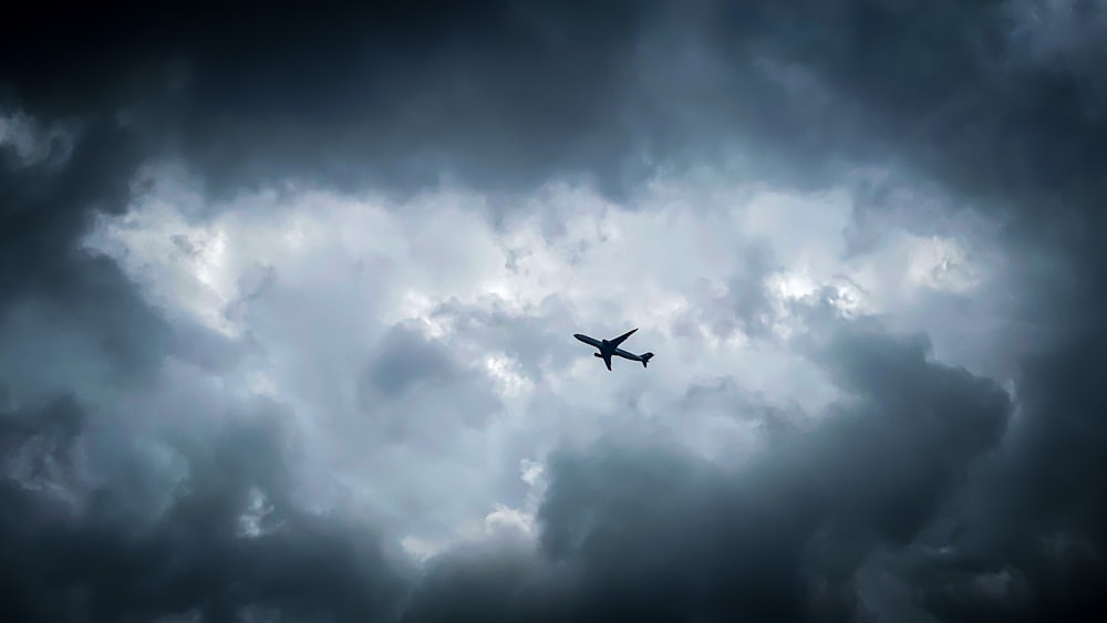 airplane flying under white clouds during daytime