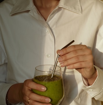 person in white button up shirt holding clear drinking glass with green liquid