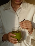 person in white button up shirt holding clear drinking glass with green liquid