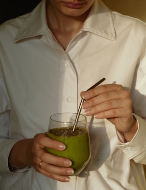 person in white button up shirt holding clear drinking glass with green liquid