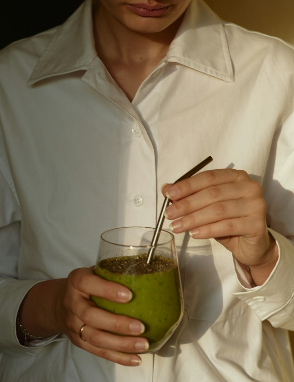 흰색 버튼 업 셔츠를 입은 사람이 녹색 액체가 든 투명한 음료수 유리를 들고 있다