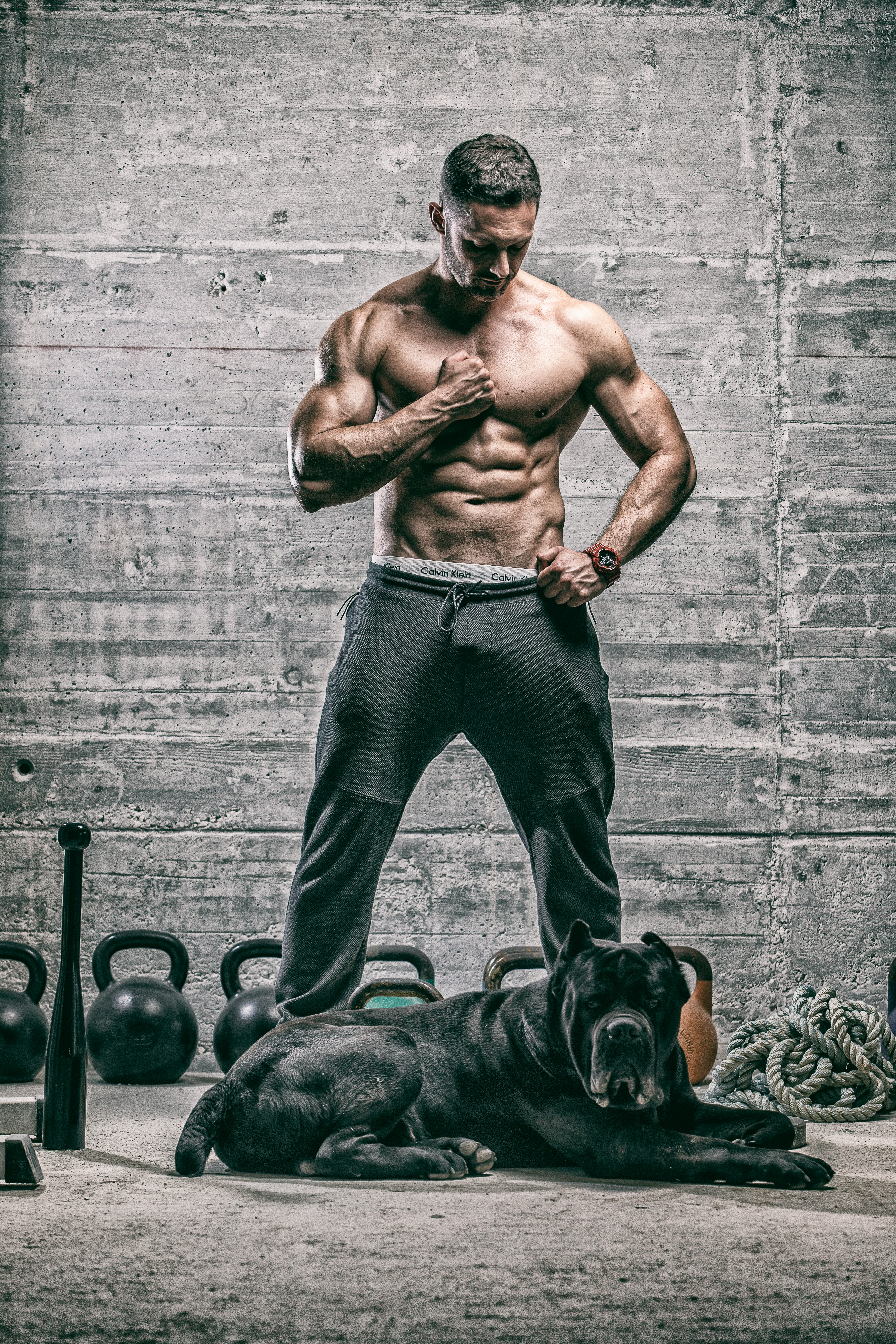 topless man in black pants standing beside black short coated dog