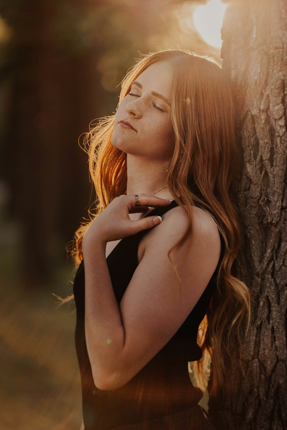 woman in black tank top leaning on brown tree