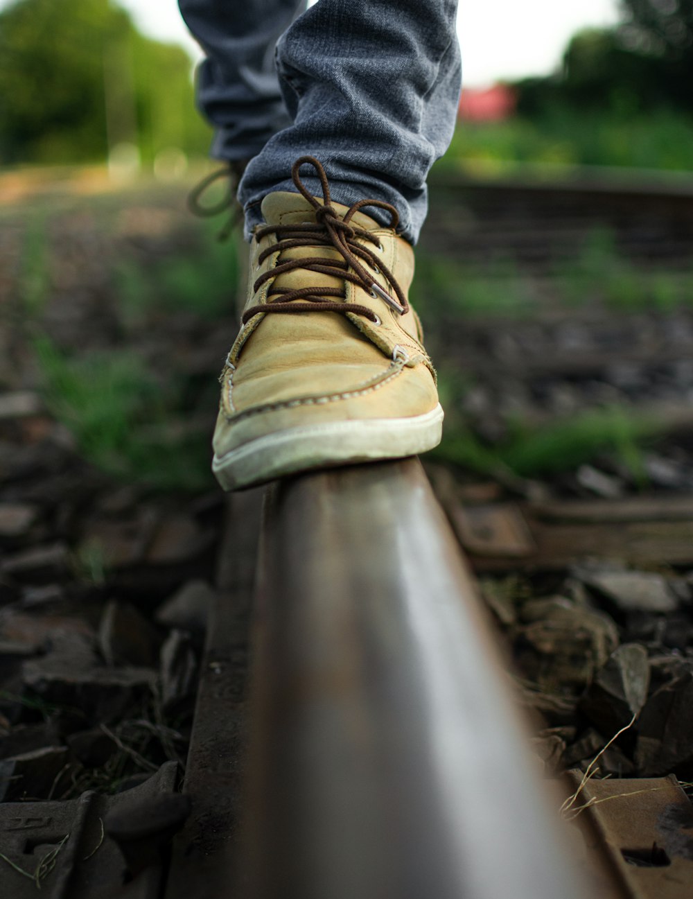 person in blue denim jeans and brown hiking shoes standing on brown wooden rail during daytime