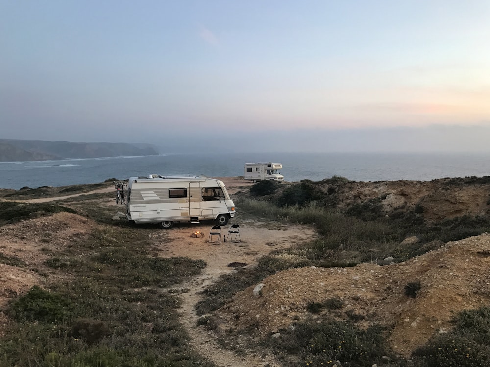 昼間の青空の下、茶色の野原に白と茶色のRV