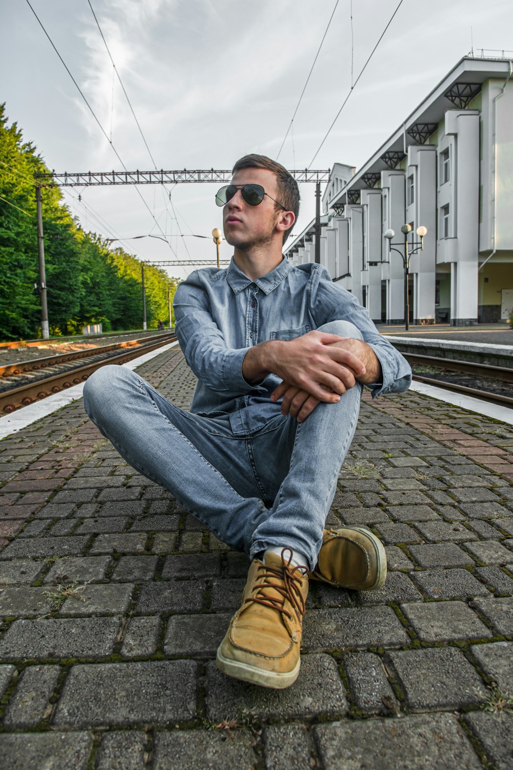 man in blue denim jacket and blue denim jeans sitting on brown brick floor