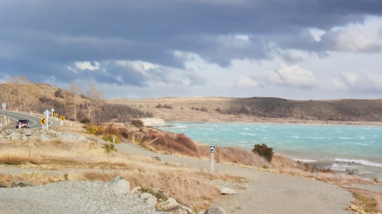 person standing on brown sand near body of water during daytime in Lake Pukaki New Zealand