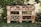 A garden insect hotel constructed from wooden pallets and filled with various natural materials like logs, bamboo, and pinecones. It is situated outdoors, surrounded by greenery and a wire fence. The structure is detailed with rows and compartments for different insects.