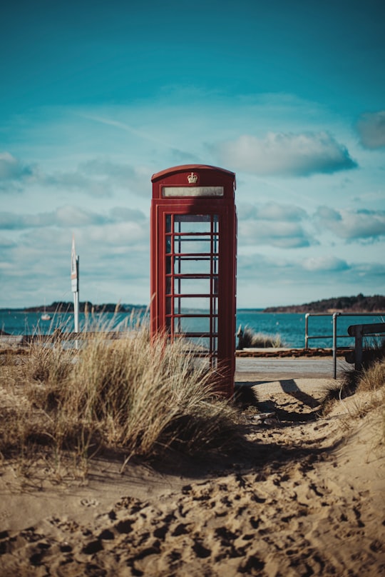 red telephone booth on brown sand under blue sky during daytime in Poole Harbour United Kingdom