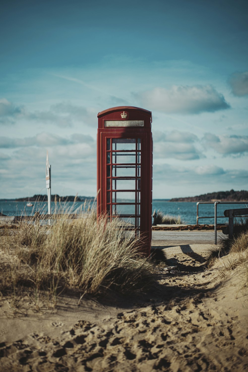 Cabina telefonica rossa su sabbia marrone sotto cielo blu durante il giorno