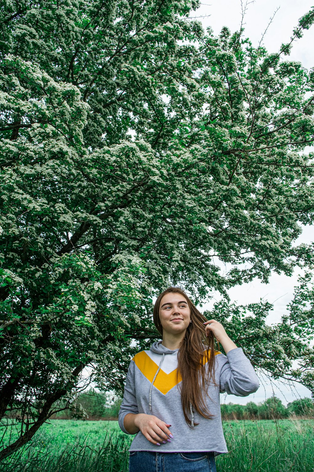 woman in gray jacket standing under green tree during daytime