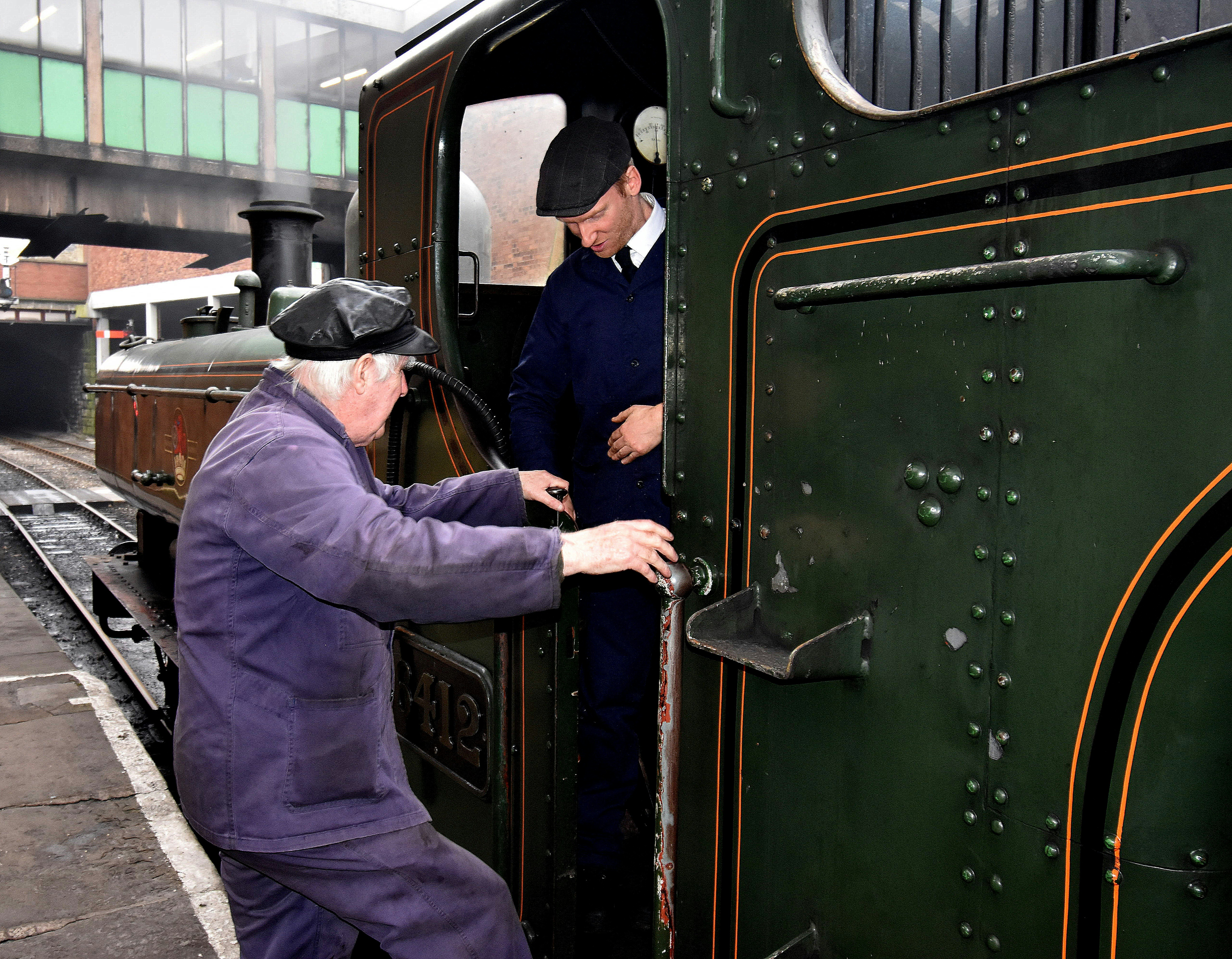 man in blue jacket and black pants wearing black hat standing beside black train during daytime