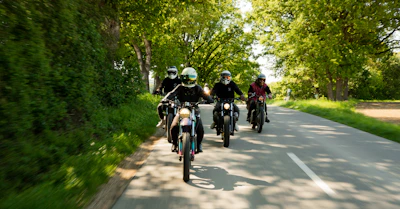 A group of travelers riding Royal Enfield motorcycles along a scenic coastal road in Ranong, Thailand.