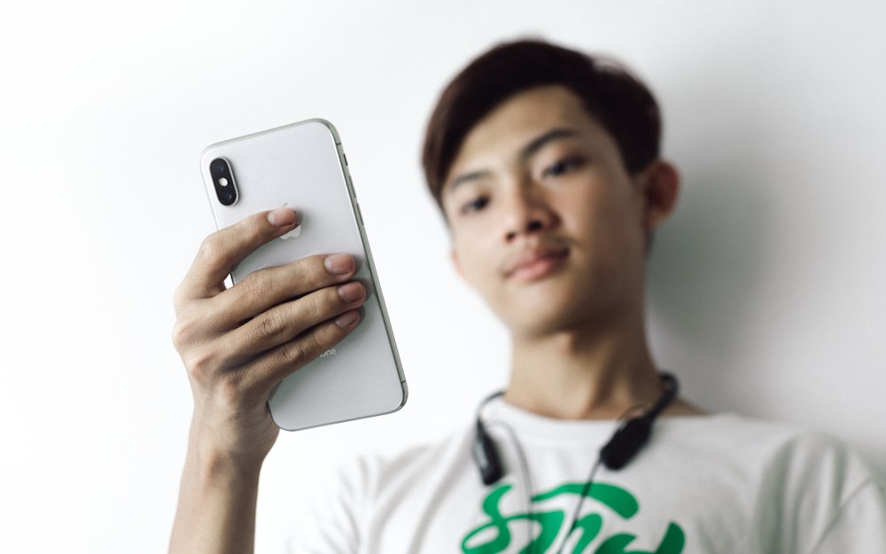 シルバーのiPhone 6を手にする白いクルーネックシャツを着た男