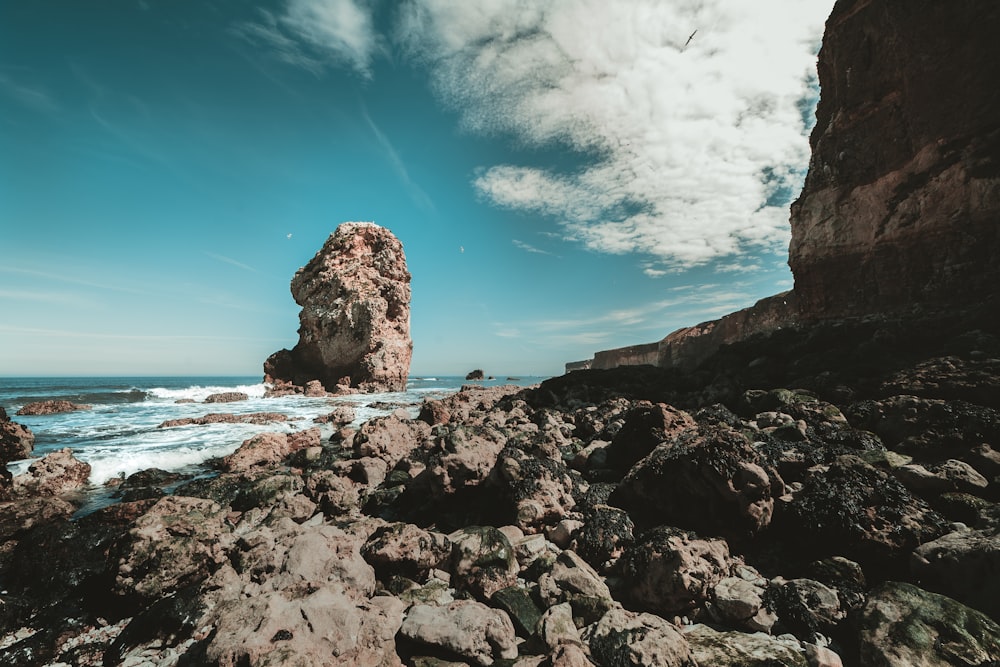Formazione rocciosa marrone sulla riva del mare sotto il cielo blu e le nuvole bianche durante il giorno