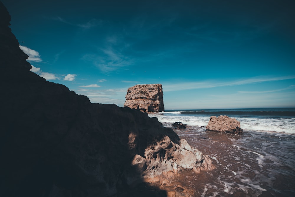 brown rock formation on sea under blue sky during daytime