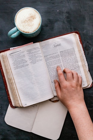 Close-up of a hand holding a Kingdom Echoes devotional book with a warm coffee cup nearby.