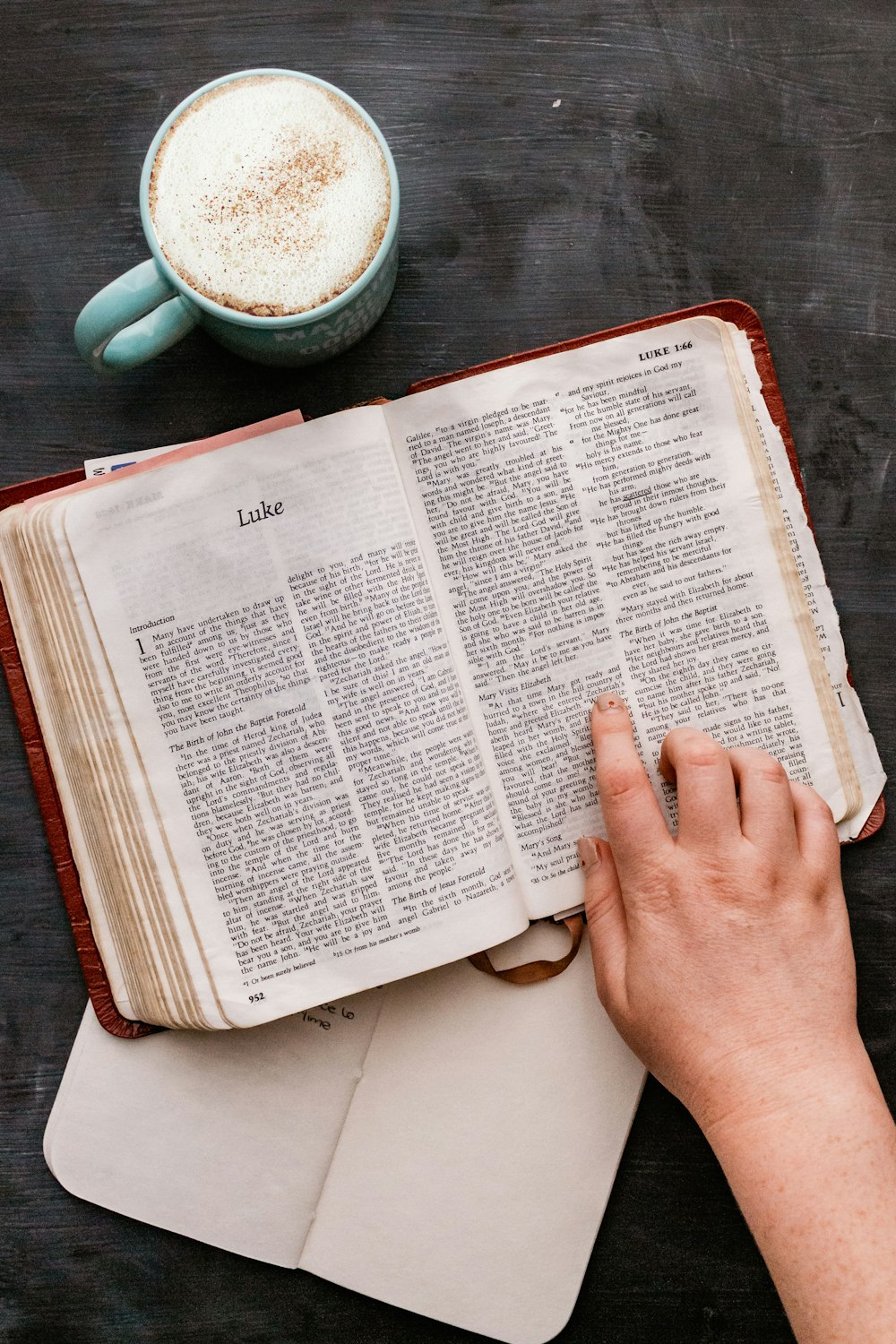 person holding book page near white ceramic mug with coffee